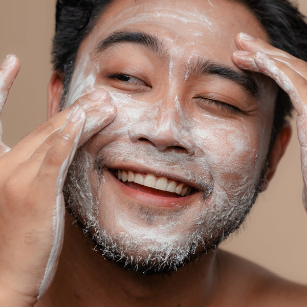 Man applying a facial mask with a neutral background