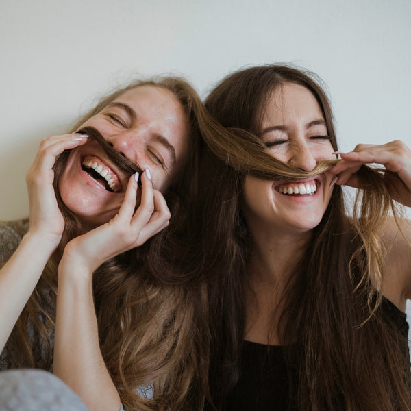 Two women laughing and playing with each other's hair.